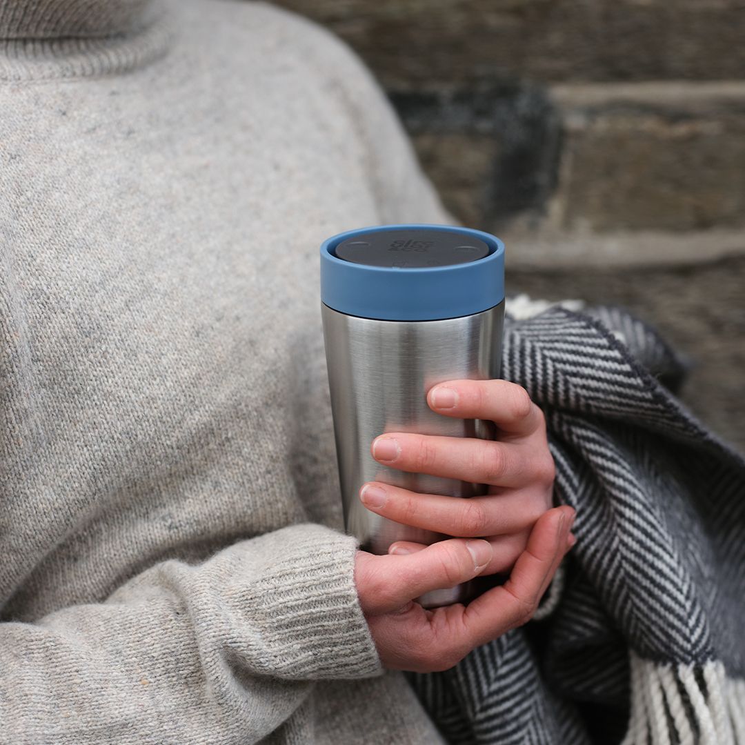 woman holding steel reusable cup with blue lid